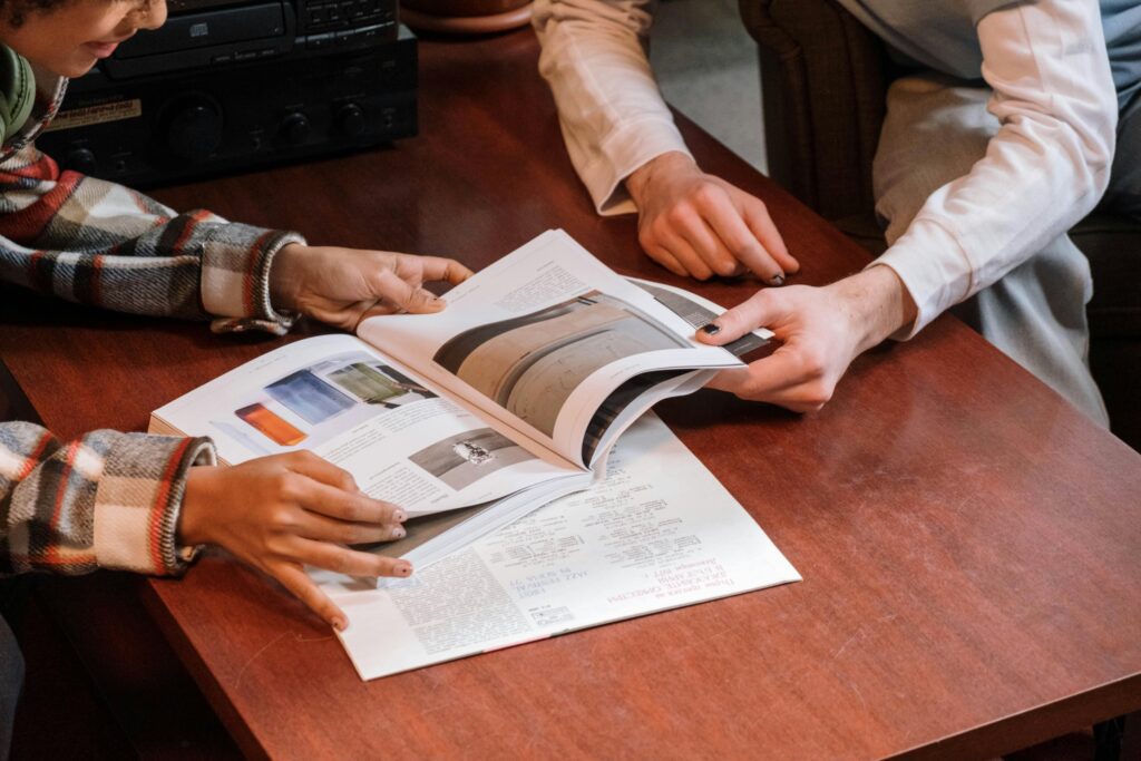 Two people's hands turning the pages of a magazine with interior design images, symbolizing the collaborative design process and personalized experience Brownhill Homes offers from conceptualization to completion.