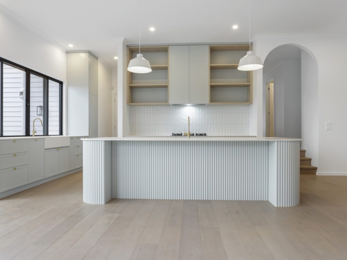 A modern kitchen with white cabinets, a light-colored island, pendant lights, and an arched doorway, symbolizing the quality materials and expert craftsmanship Brownhill Homes uses in designing and constructing custom homes.