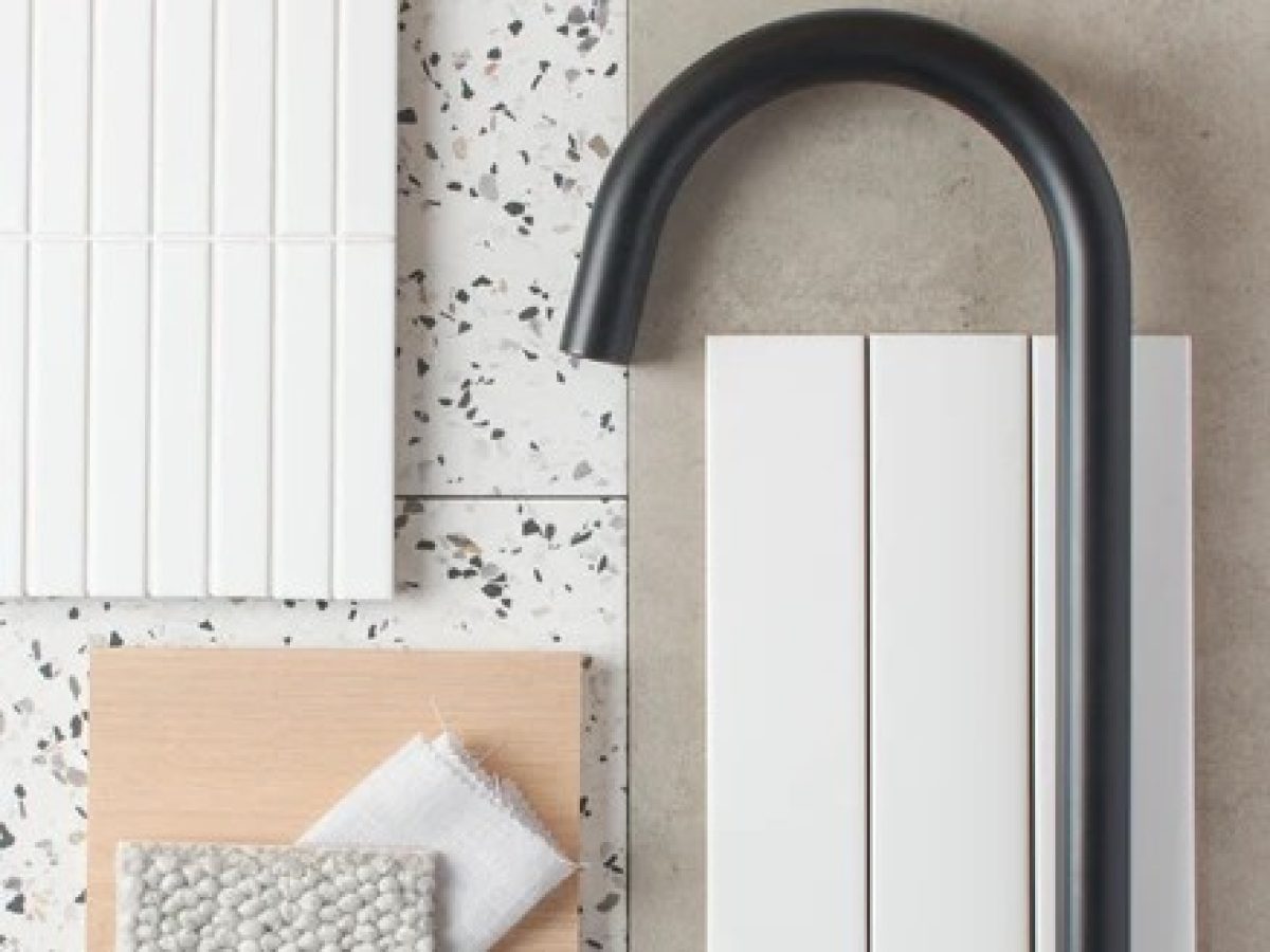 Close-up photograph of a mood board or design sample board. The board features various materials and textures, including white tiles with a grooved pattern, a light-colored wooden sample, a textured gray fabric swatch, and a dark, curved metal fixture, possibly a tap or handle. The materials are arranged in a collage style, suggesting a design palette. The image represents Brownhill Homes' process of "Understanding Your Vision," as described in the accompanying text, which focuses on consultations and understanding client preferences.