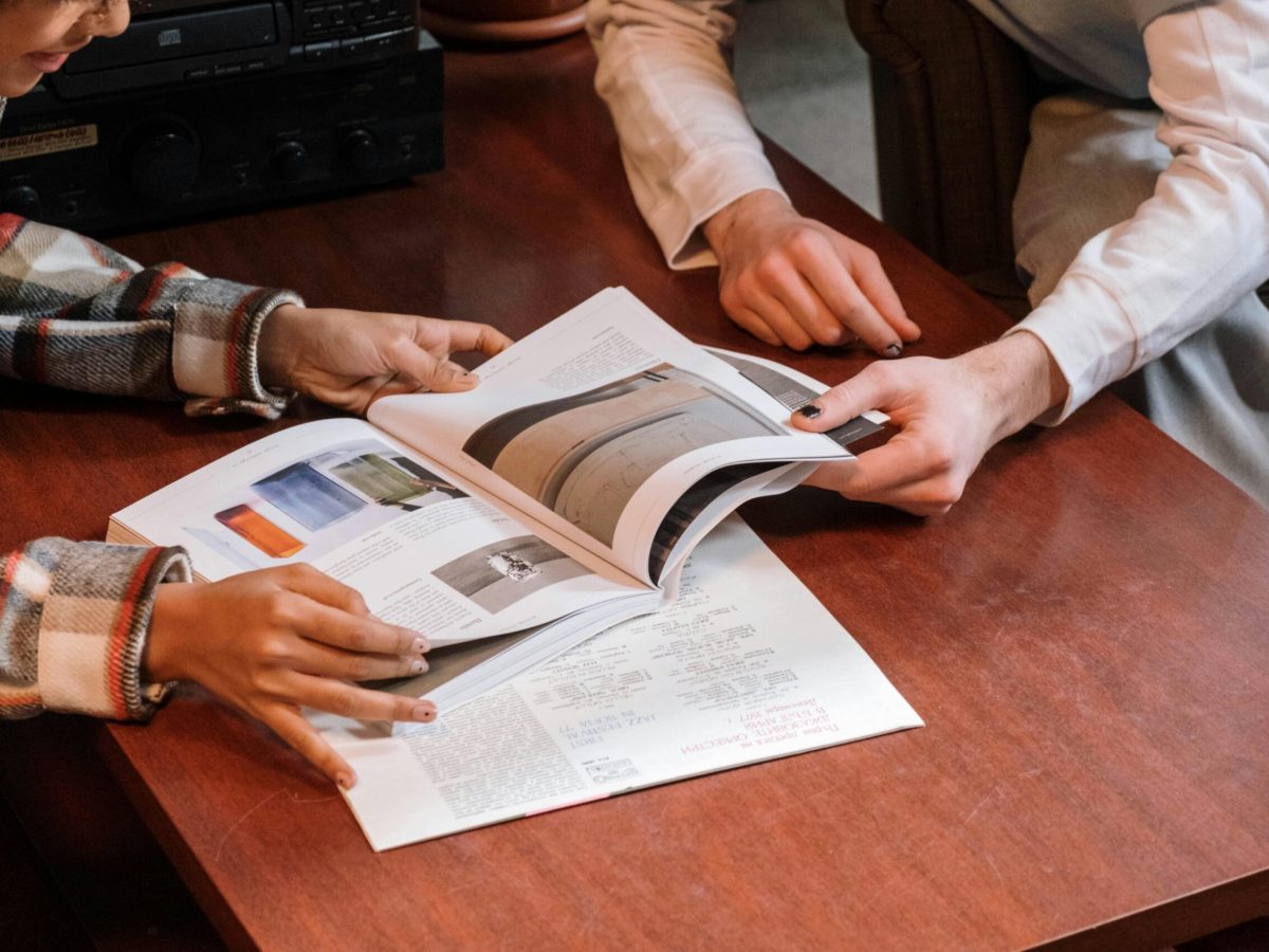 Two people's hands turning the pages of a magazine with interior design images, symbolizing the collaborative design process and personalized experience Brownhill Homes offers from conceptualization to completion.