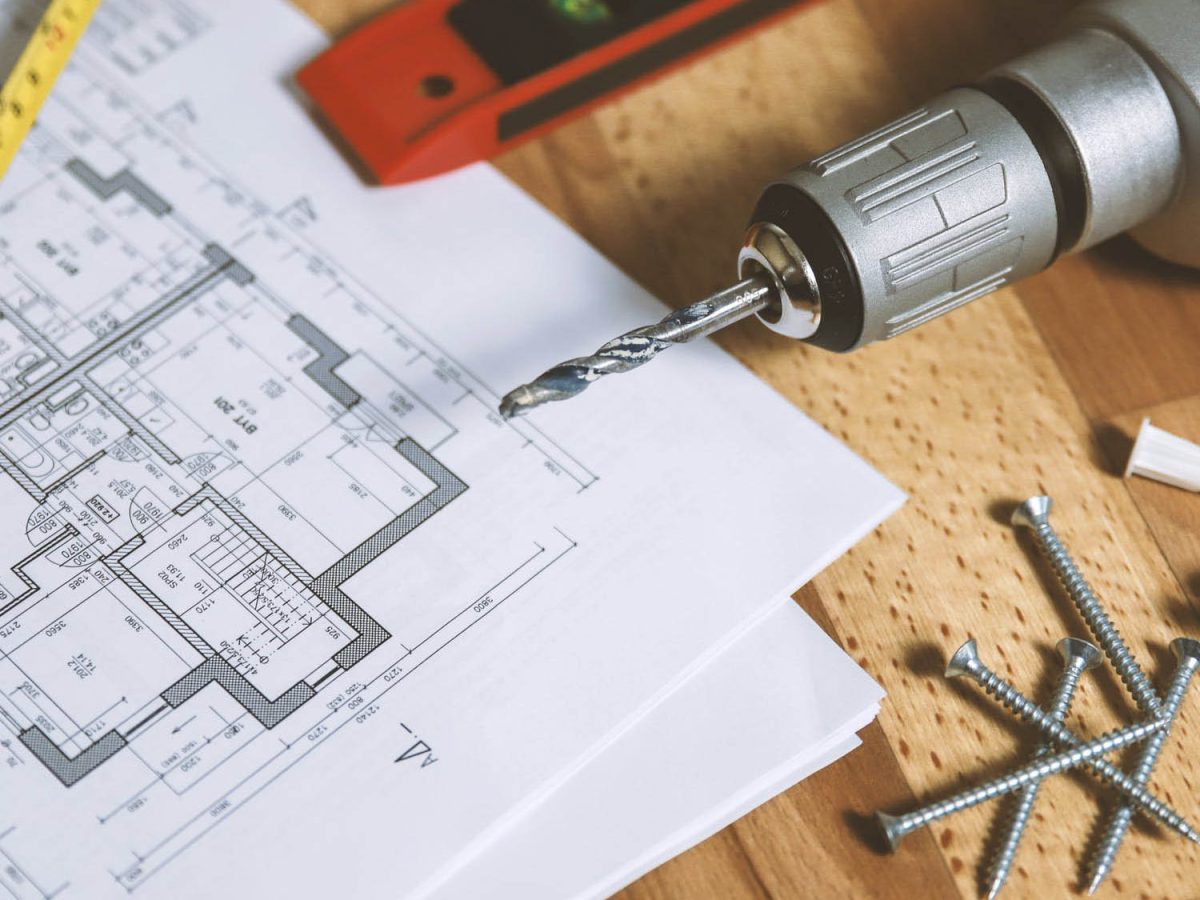 A close-up of a drill, screws, a level, a tape measure, and chalk on top of architectural blueprints, representing Brownhill Homes' focus on exceeding client expectations and fulfilling their vision.