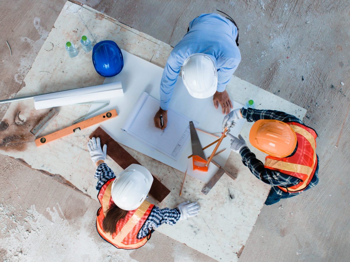 An aerial view of a construction worker in a blue hard hat working on plans with tools like a hammer, level, and measuring tape, representing the experienced custom home builders team at Brownhill Homes.
